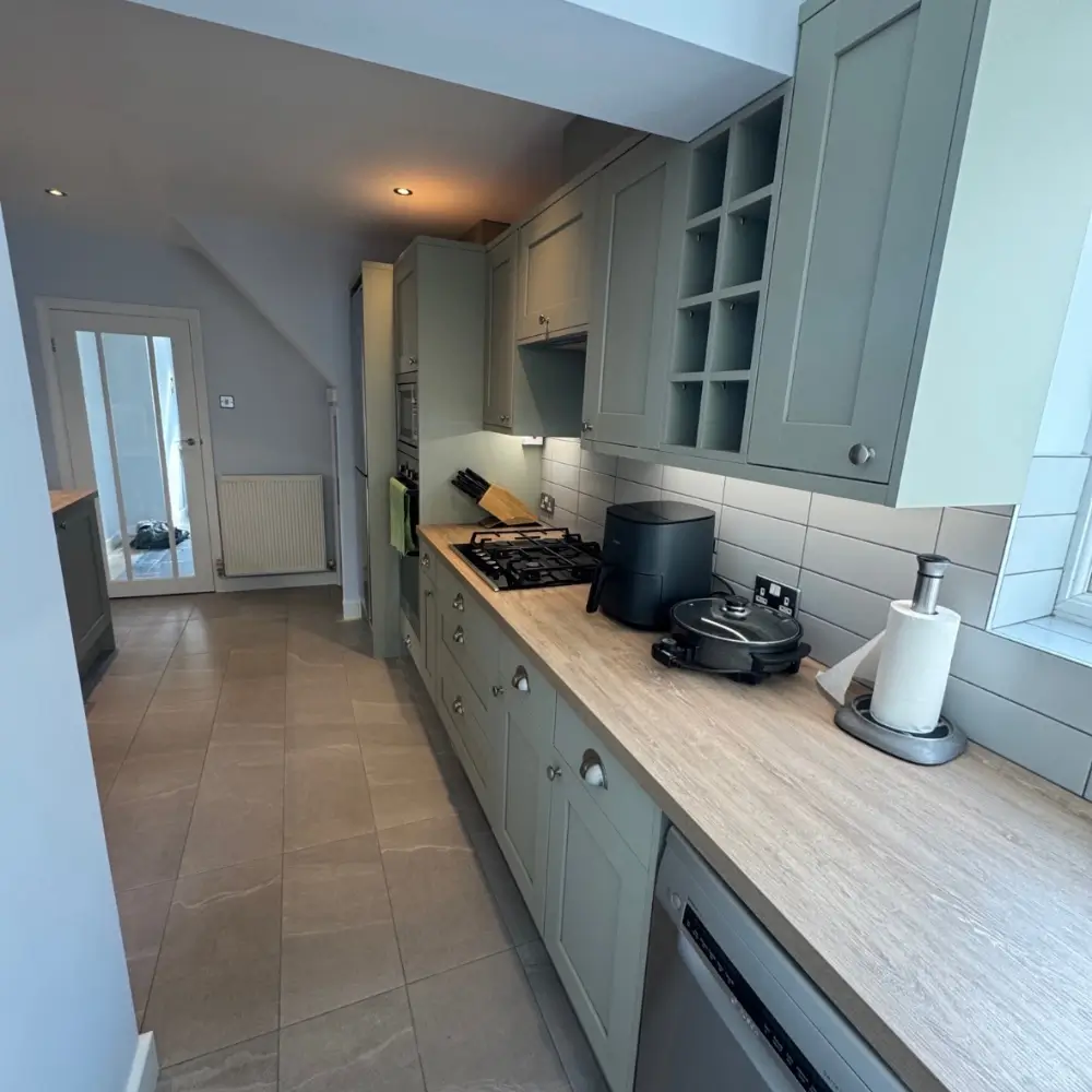 Modern galley kitchen with sage green cabinets, wooden worktop, and integrated appliances by Spera Restoration.
